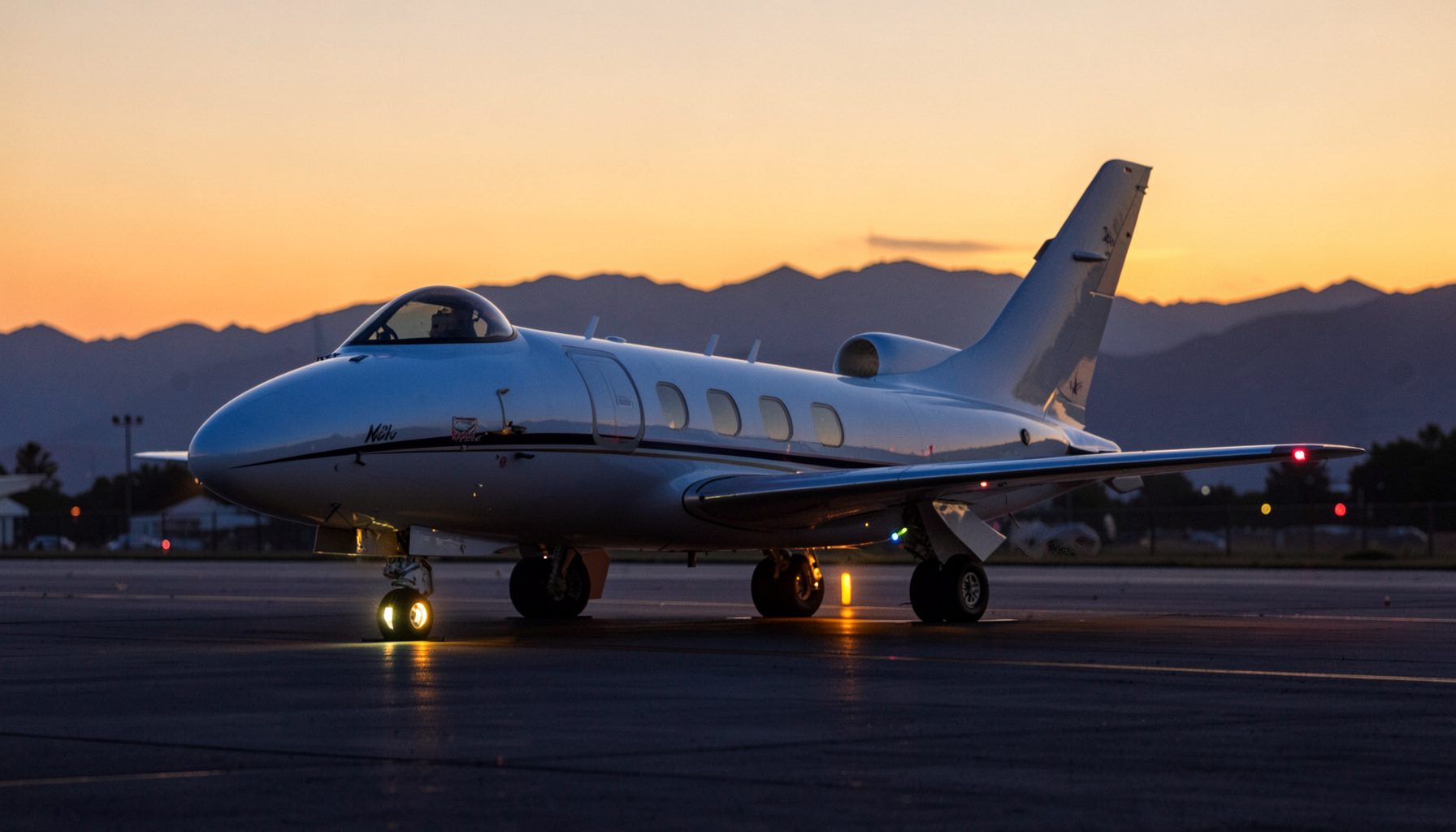 A sleek Cirrus aircraft on the ramp at dusk, navigation lights glowing, distant mountains silhouetted against an amber sky